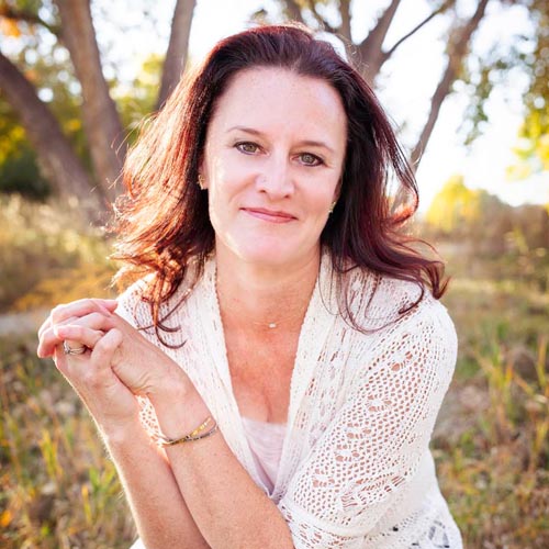 A woman wearing glasses and a green coat holds a white paper